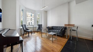 Een moderne woonkamer met een piano, een salontafel met glazen blad, een grijze bank en twee fauteuils.