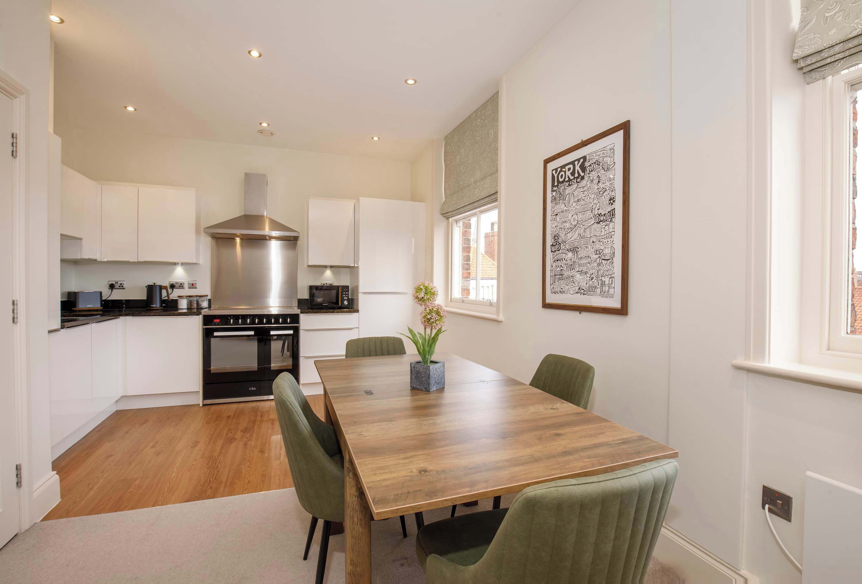 A modern kitchen with white cabinets, a stainless steel range hood, and a wooden dining table with chairs.