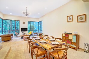 A spacious dining area with a long wooden table, multiple chairs, and a television mounted on the wall. - ELIVAAS Villa 39 Serene 6BHK with Pool (Lonavala)