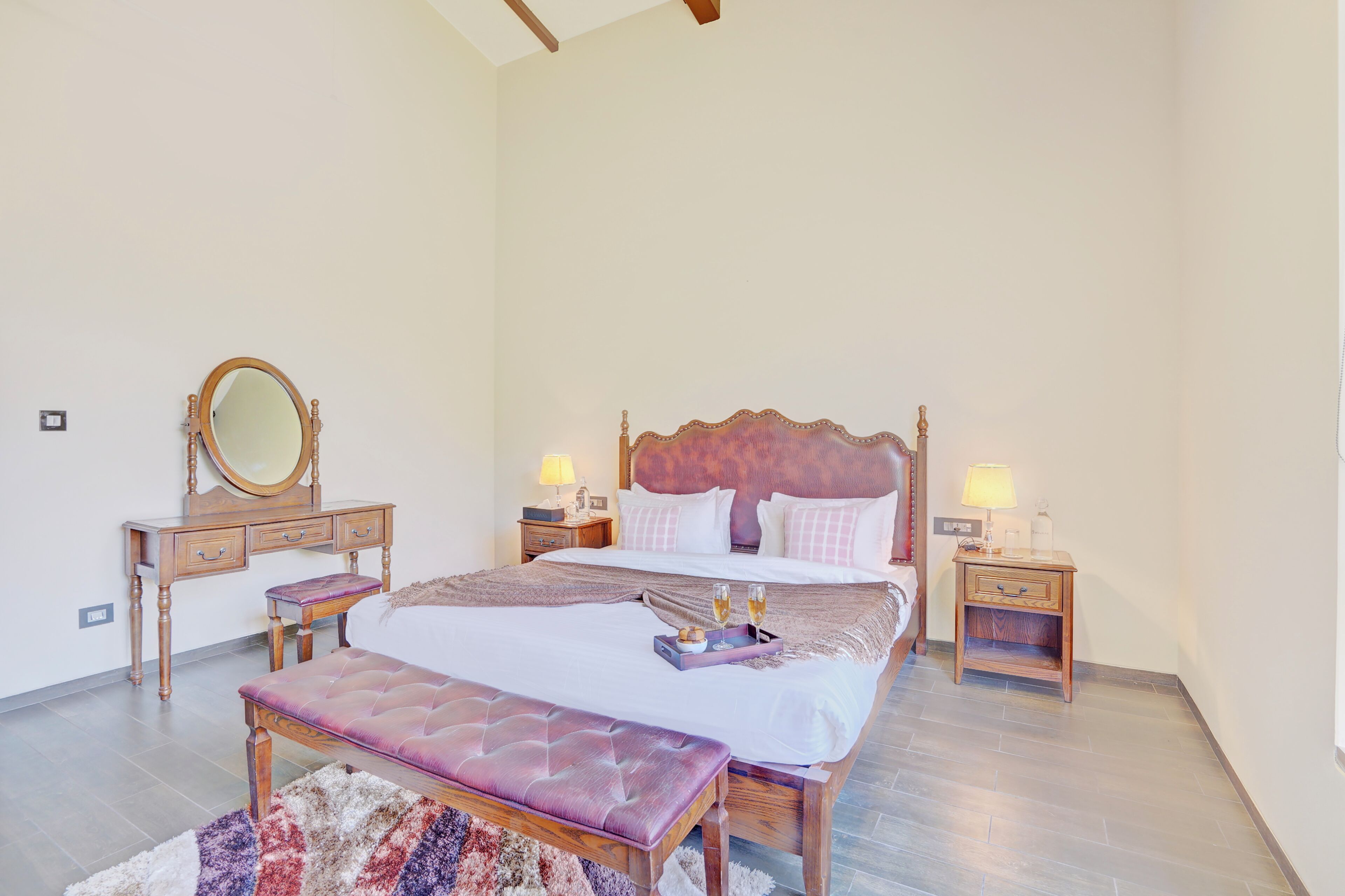 Quarto com cama, mesas de cabeceira, espelho, banco e tapete.
