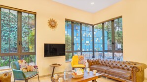 A living room with a sofa, a chair, a coffee table, and large windows. - ELIVAAS Villa 39 Serene 6BHK with Pool (Lonavala)