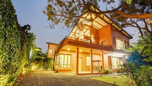 A two-story house with a balcony, large windows, and a well-lit driveway. - ELIVAAS Villa 39 Serene 6BHK with Pool (Lonavala)