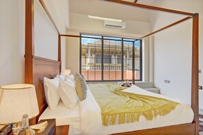 A hotel room with a four-poster bed, a nightstand with a lamp, and a view of a building through a large window. - ELIVAAS Villa 39 Serene 6BHK with Pool (Lonavala)