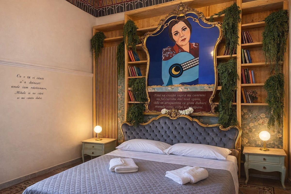 Un dormitorio con una cama grande, dos mesitas de noche, una pared con un retrato enmarcado y una estantería con plantas.
