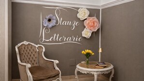 Une pièce comprenant un fauteuil capitonné, une petite table ronde avec un livre et des fleurs, et un mur orné d’un panneau décoratif.