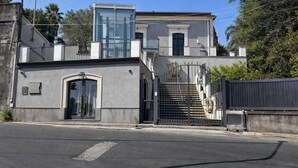Un bâtiment moderne à deux étages, doté d’une véranda en verre, d’une entrée sécurisée par un portail et d’un escalier apparent.