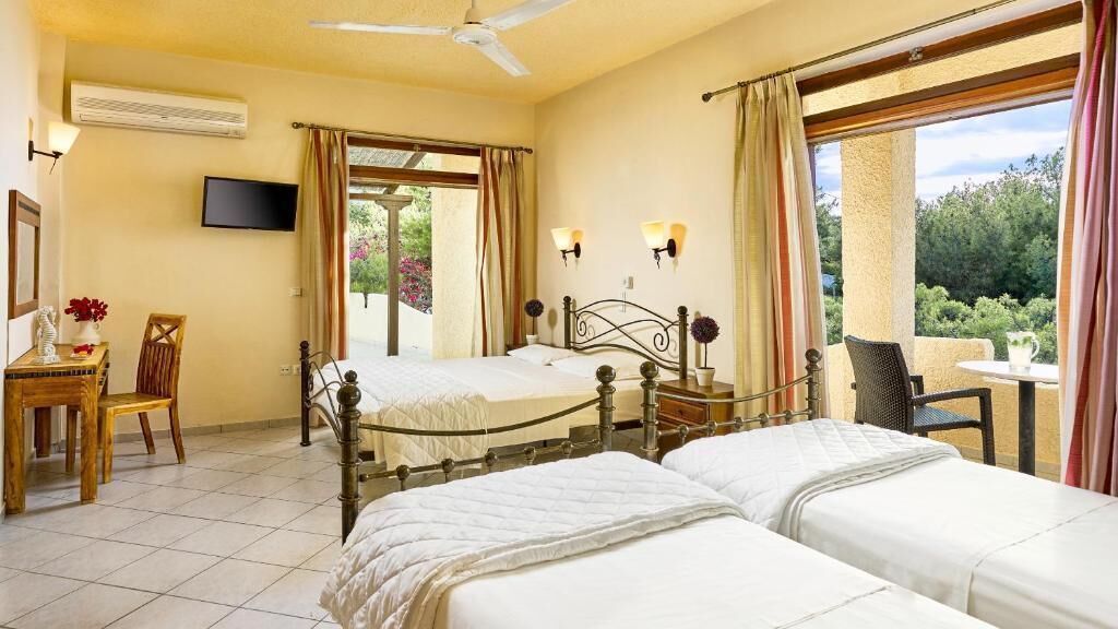 A hotel room with two beds, a TV, a desk with a chair, and a view of greenery outside.