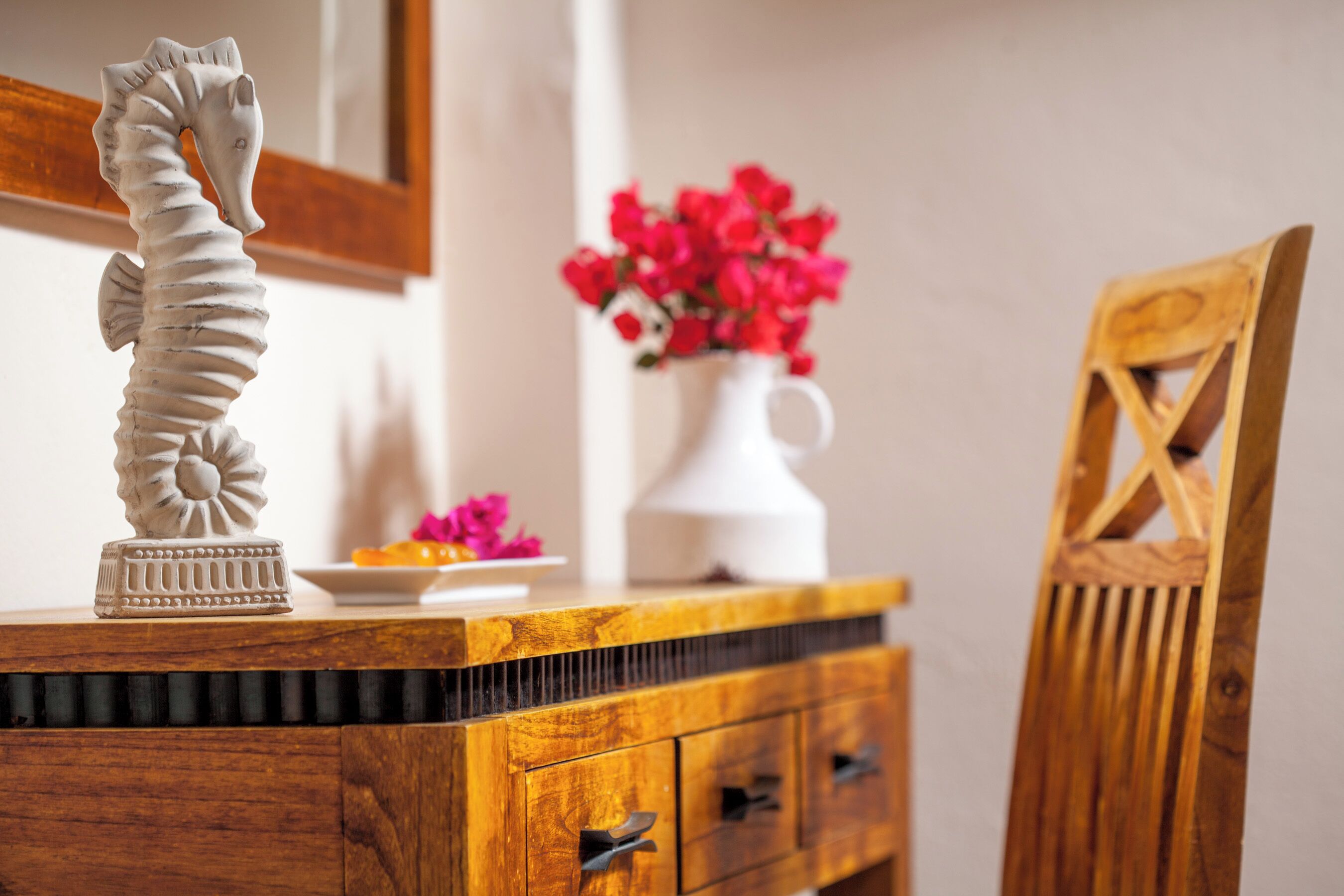 A wooden dresser with a decorative seahorse, a white vase with red flowers, and a wooden chair.