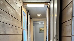A wooden hallway with a door leading to a room, a ceiling light, and a framed picture on the wall. - Coastal Trail Cottages - Captain Jack's Lookout (Morell)