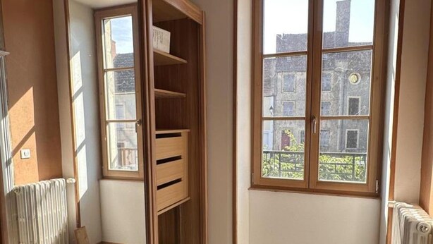 Une pièce d ’angle avec un meuble en bois, un radiateur et une fenêtre donnant sur des immeubles.