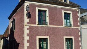 Un immeuble de deux étages doté d’une façade à motifs, de cadres de fenêtres verts et d’un petit balcon situé à l’étage supérieur.