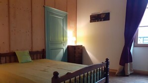 Une chambre à coucher avec un lit en bois, une porte verte, une commode et une fenêtre avec des rideaux.