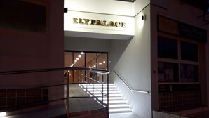 Entrada de un edificio con un letrero que dice 'ELYPALACE', una escalera con barandillas de metal y un felpudo estampado en la parte inferior.