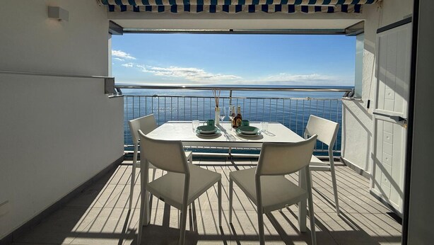 Un balcón con mesa y sillas, vista al mar y un toldo a rayas.