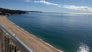 Vista costera con playa, cielo despejado y colinas a lo lejos.
