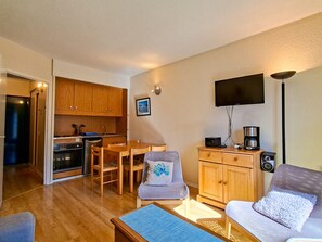 A compact living space with a kitchenette, a dining area, a sofa, and a TV mounted on the wall. - Bright studio with balcony - 4 guests (Flaine)
