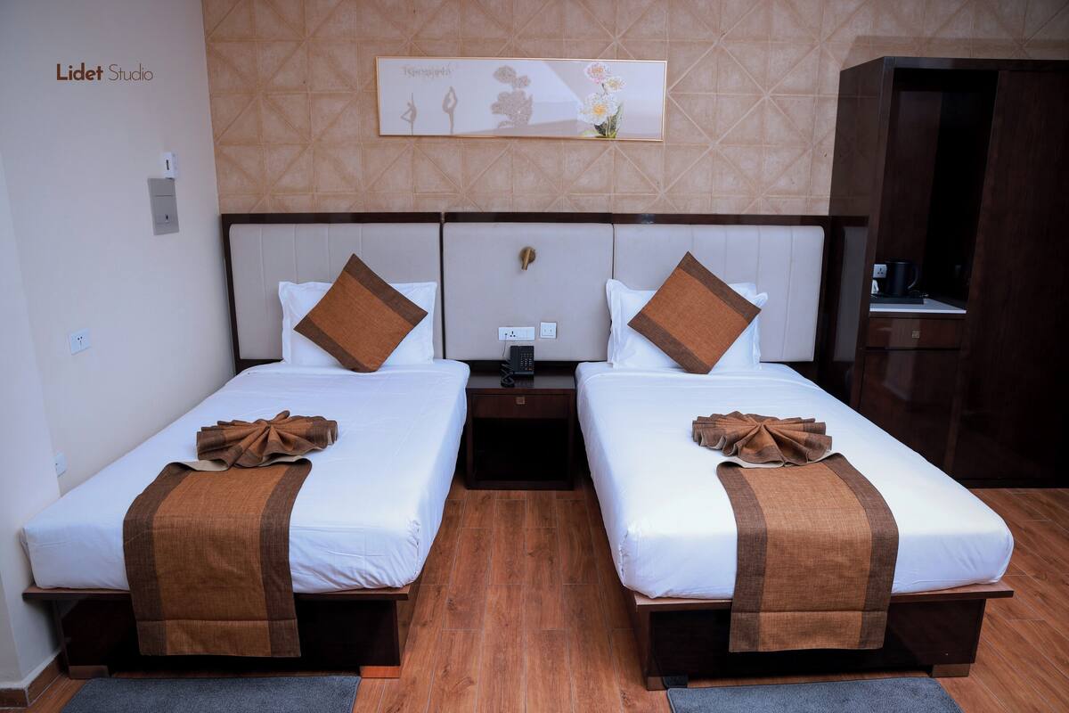 A hotel room with two beds, a headboard with a control panel, a small table, and a cabinet.