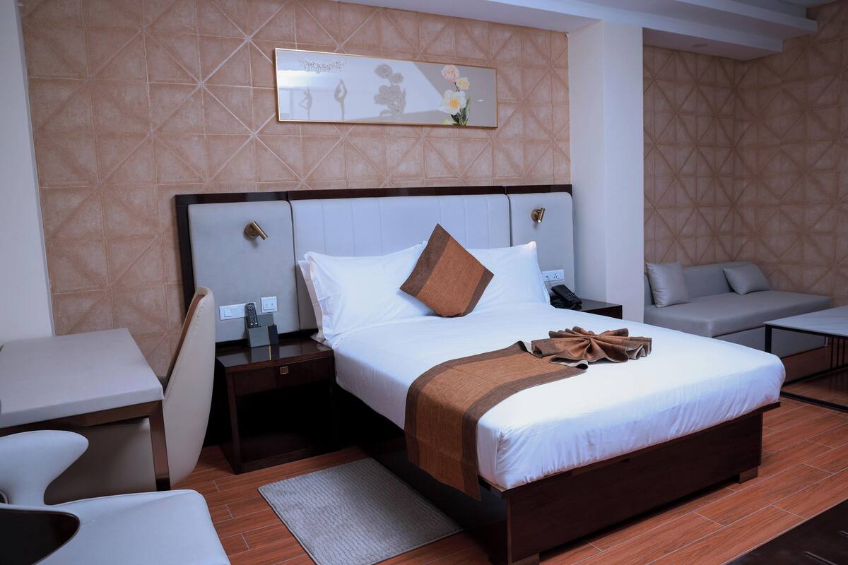 A hotel room with a large bed, a bedside table, a chair, a desk, and a wall-mounted artwork.