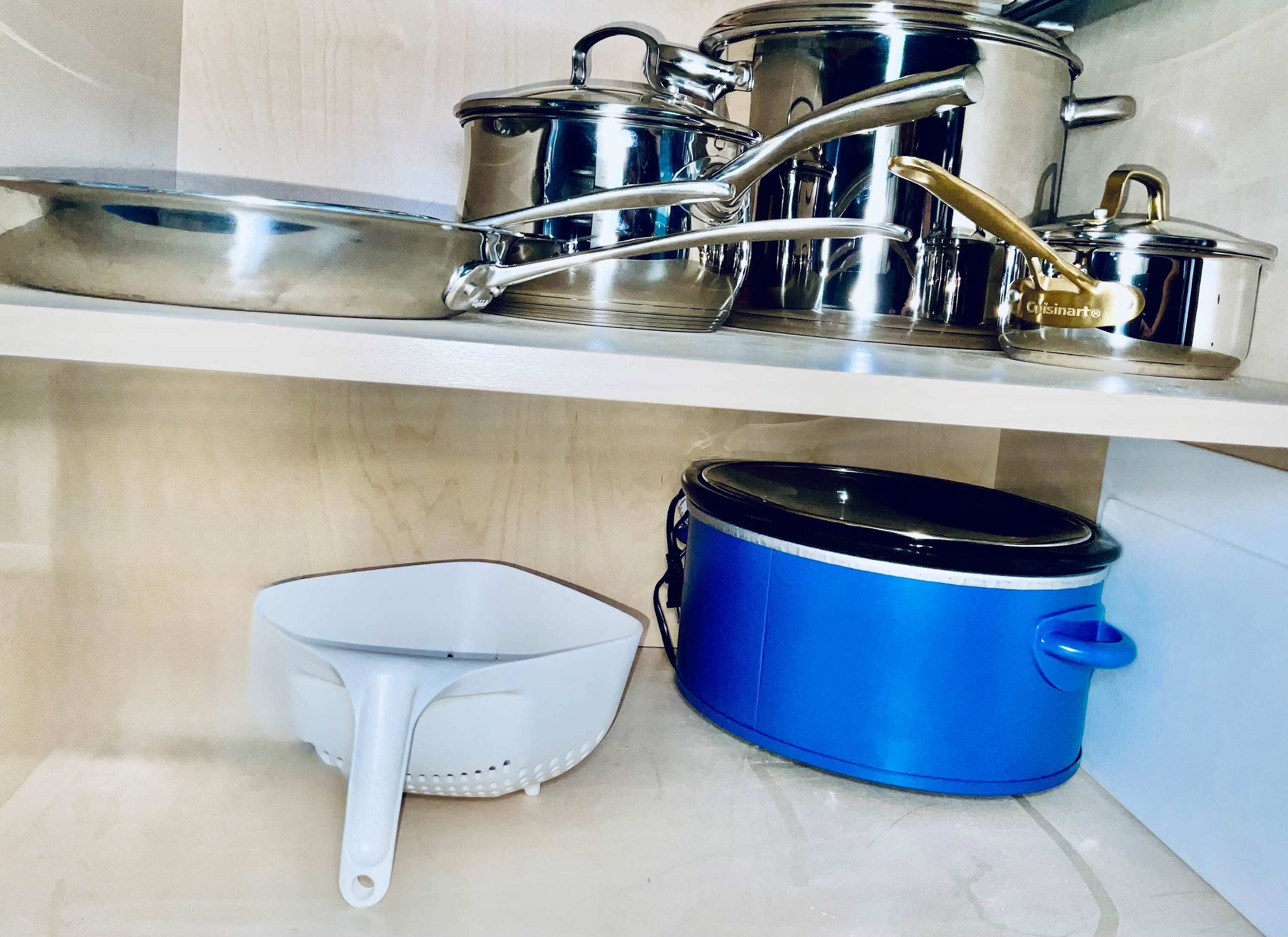 Eine Küche mit Edelstahlkochgeschirr auf einem Regal, einem blauen Slow-Cooker und einem weißen Sieb auf der Arbeitsfläche.