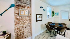 A dining area with a round table, chairs, and a wall-mounted mirror. - Hot Tub Tideaway Walkable (Galveston)