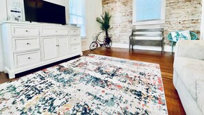 A living room with a white dresser, a television, a patterned rug, a bicycle, and a bench. - Hot Tub Tideaway Walkable (Galveston)