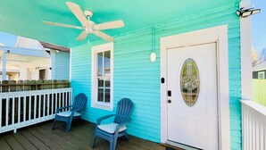A turquoise house with a white door, a ceiling fan, and two chairs on the porch. - Hot Tub Tideaway Walkable (Galveston)