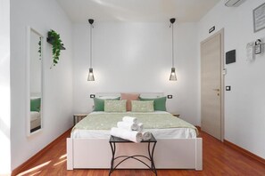 A bedroom with a bed, two pendant lights, a bedside table with towels, a mirror, and a door. - Hotiday La Spezia Quiet Night (La Spezia)