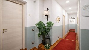 A hallway with a red carpet, a potted plant, a wall-mounted lamp, and a door with a brass handle. - Hotiday La Spezia Quiet Night (La Spezia)