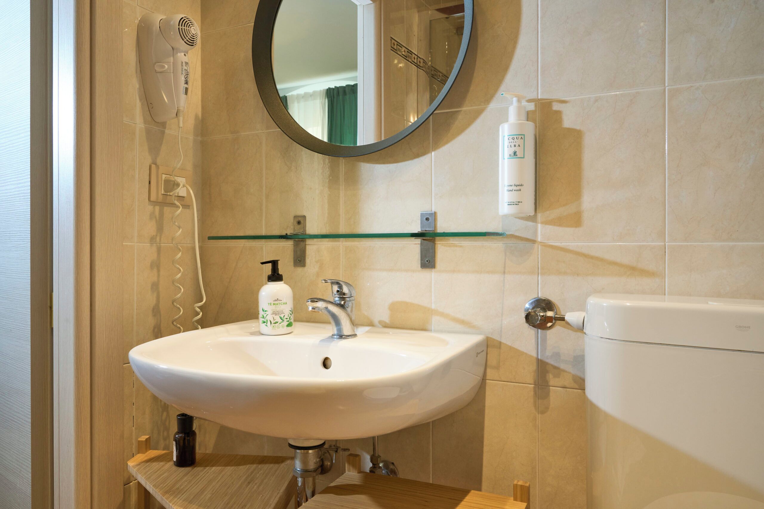 A bathroom with a white sink, a mirror, a hairdryer, and toiletries on the wall.