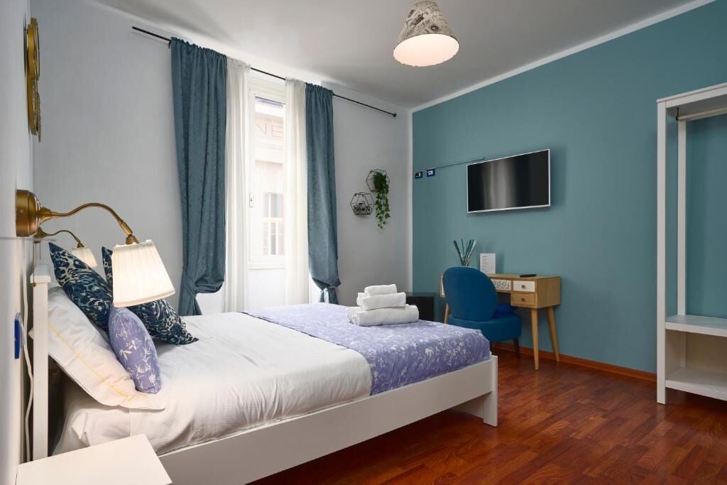 A bedroom with a bed, bedside lamps, a desk, a chair, a TV, and a wardrobe.