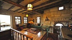Un intérieur rustique avec des poutres apparentes, une cheminée en pierre, un canapé vert et une table à manger en bois.