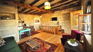 Un intérieur rustique avec des murs en pierre, un plafond en bois, un coin cuisine, un canapé vert et un fauteuil rouge.
