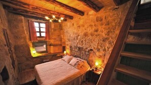Une pièce rustique avec un lit, une fenêtre avec des rideaux, un mur en pierre et une échelle en bois.