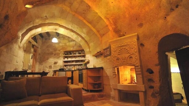 Interior com paredes de pedra, lareira, sofá e prateleira com diversos objetos.
