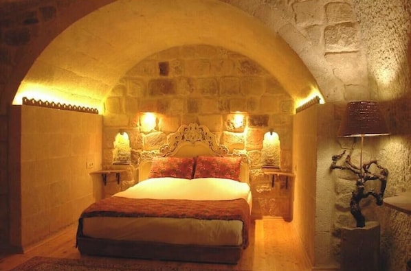 A bedroom with a stone arch ceiling, a bed with a headboard, two bedside lamps, and a wall-mounted lamp.