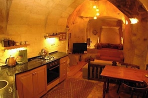 A cozy kitchen with a dining area, stone walls, and a fireplace.