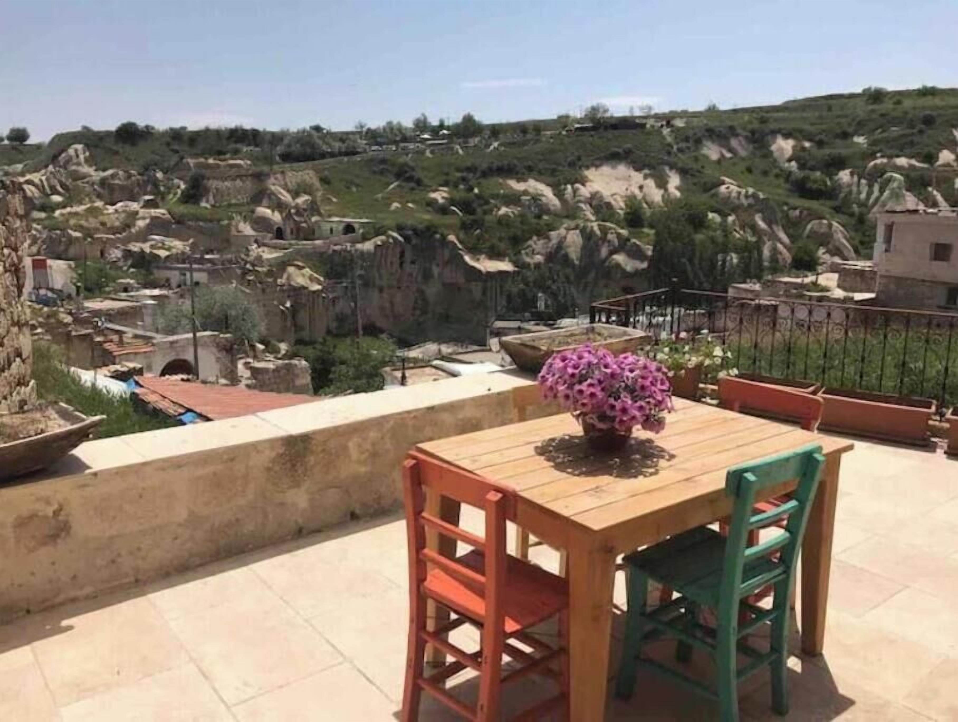 Ein Holztisch mit Stühlen auf einem Balkon mit Blick auf eine felsige Landschaft und Gebäude.