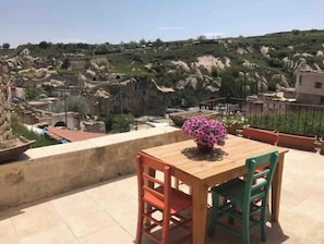 A wooden table with chairs on a balcony overlooking a rocky landscape with buildings.