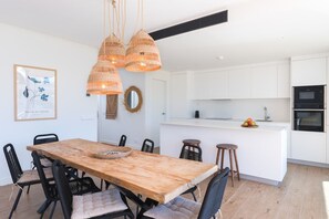 Eine moderne Küche mit weißen Schränken, einem Holztisch und Lampen aus Weidwerk.
