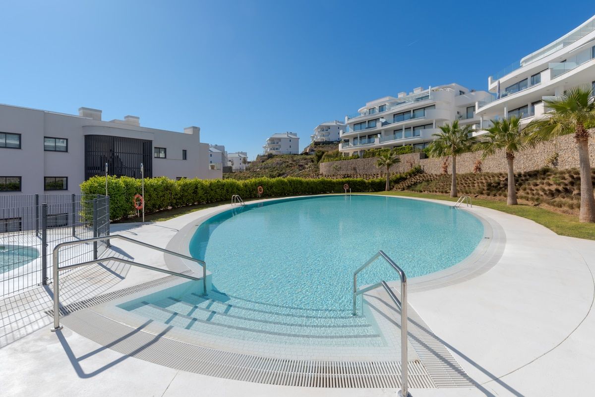 A modern swimming pool with a curved design, surrounded by a paved deck and metal railings.
