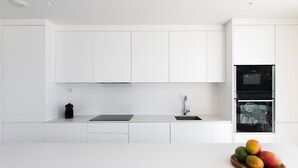 Een moderne keuken met witte kastjes, een zwarte koffiemachine, een spoelbak en een fruitschaal op het aanrecht.