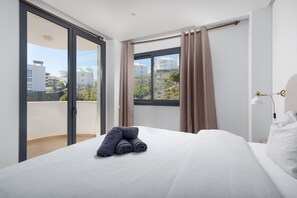 A hotel room with a bed, a window with curtains, and a view of buildings outside. - Paula Lemac | Modern Apartment with Panoramic Sea & Mountain Views & Terrace in El Higueron (Fuengirola)