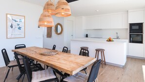 Een moderne keuken met witte kasten, een houten eettafel, zwarte stoelen, rieten hanglampen en een keukeneiland met krukken.