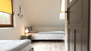 A small, single-room accommodation with a sloped ceiling, two beds, a bedside table with a lamp, and a window providing natural light. - Year-round Holiday Home With Fireplace, 3 Bedrooms (Choczewo)