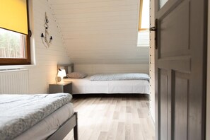 A small, single-room accommodation with a sloped ceiling, two beds, a bedside table with a lamp, and a window providing natural light. - Year-round Holiday Home With Fireplace, 3 Bedrooms (Choczewo)