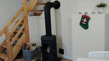 Quarto com uma lareira a lenha de madeira escura, escada de madeira, cesta de vime com lenha e uma meia de Natal verde na parede.