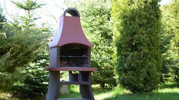 Una parrilla con chimenea, ubicada en un jardín con follaje y árboles.