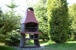 A barbecue grill with a chimney, set in a garden with greenery and trees. - Year-round Holiday Home With Fireplace, 3 Bedrooms (Choczewo)