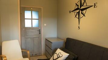 Una habitación con puerta, una silla blanca, un sofá, un pequeño armario blanco y decoración de pared con una brújula.
