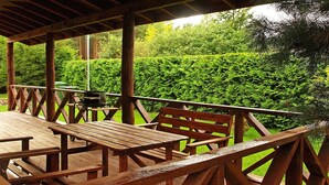 An outdoor wooden deck with picnic tables and benches, surrounded by lush greenery. - Year-round Holiday Home With Fireplace, 3 Bedrooms (Choczewo)